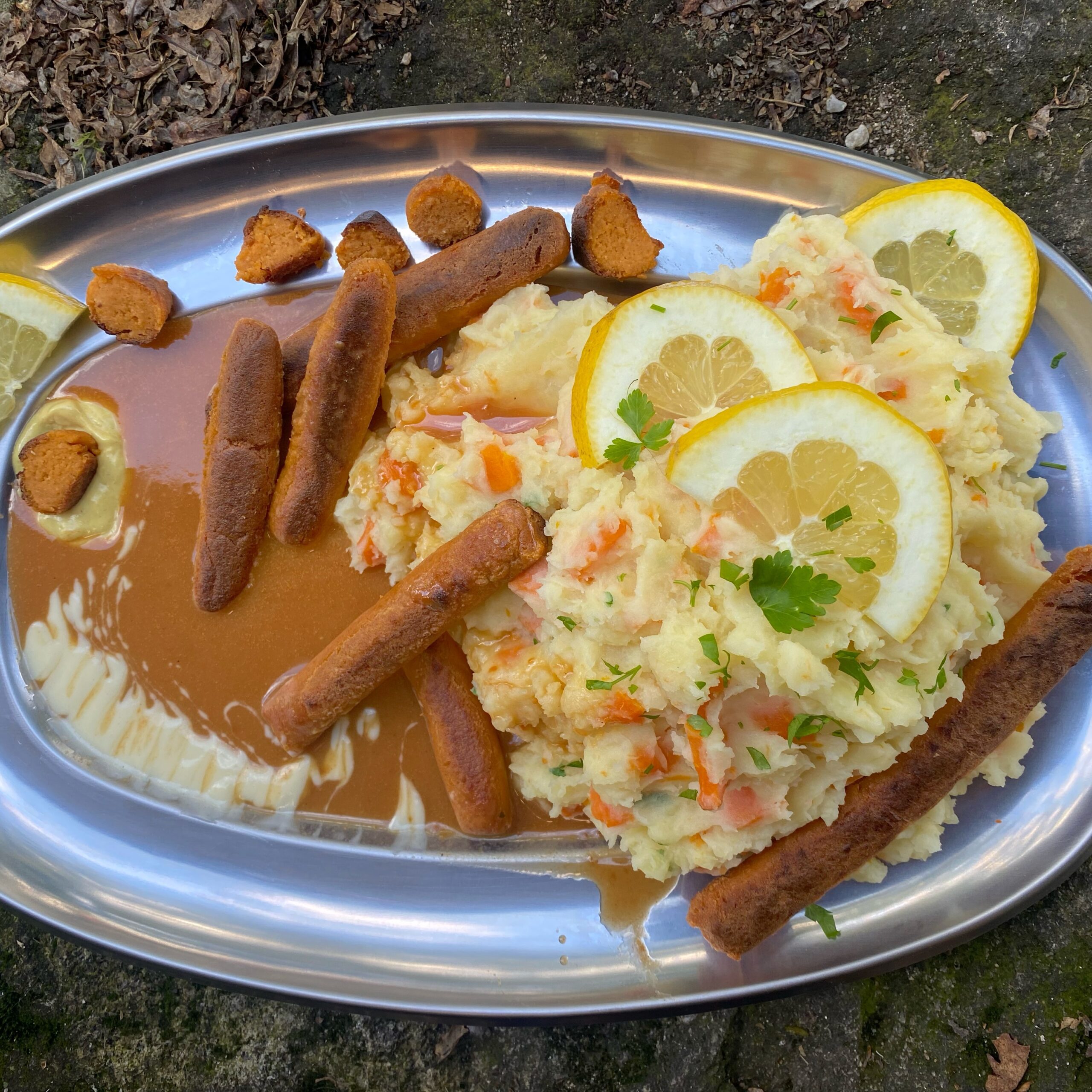 mashed potatoes and carrots and vegan sausages arranged in a mahagoni sauce on a silver plate.