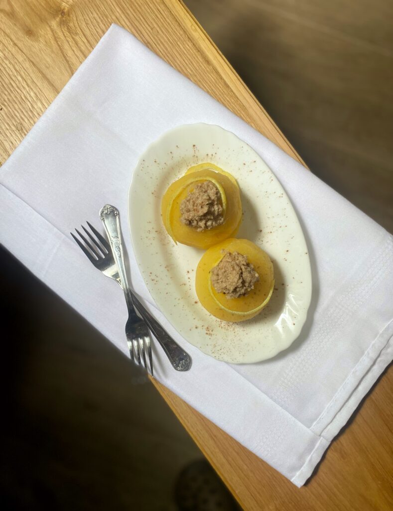 two stuffed apples on a white plate, two forks and a white cloth on a wooden surface