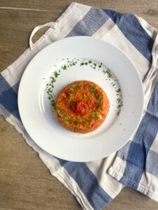 a pepper and tomato rice dish, served on a white plate with parsley garnish, on a blue and white kitchen cloth