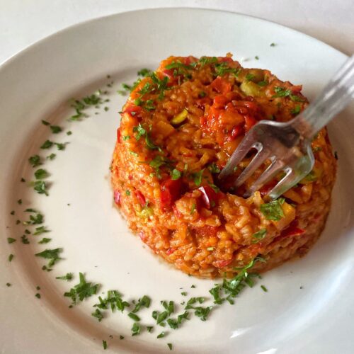 peppers and tomato rice on white plate, garnished with parsley and ajvar