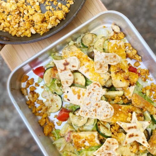 a tray full with cegetables, crispy tofu and fals eggs on a wooden table