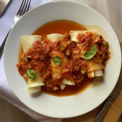 lasagne rolls in tomato sauce on a white plate