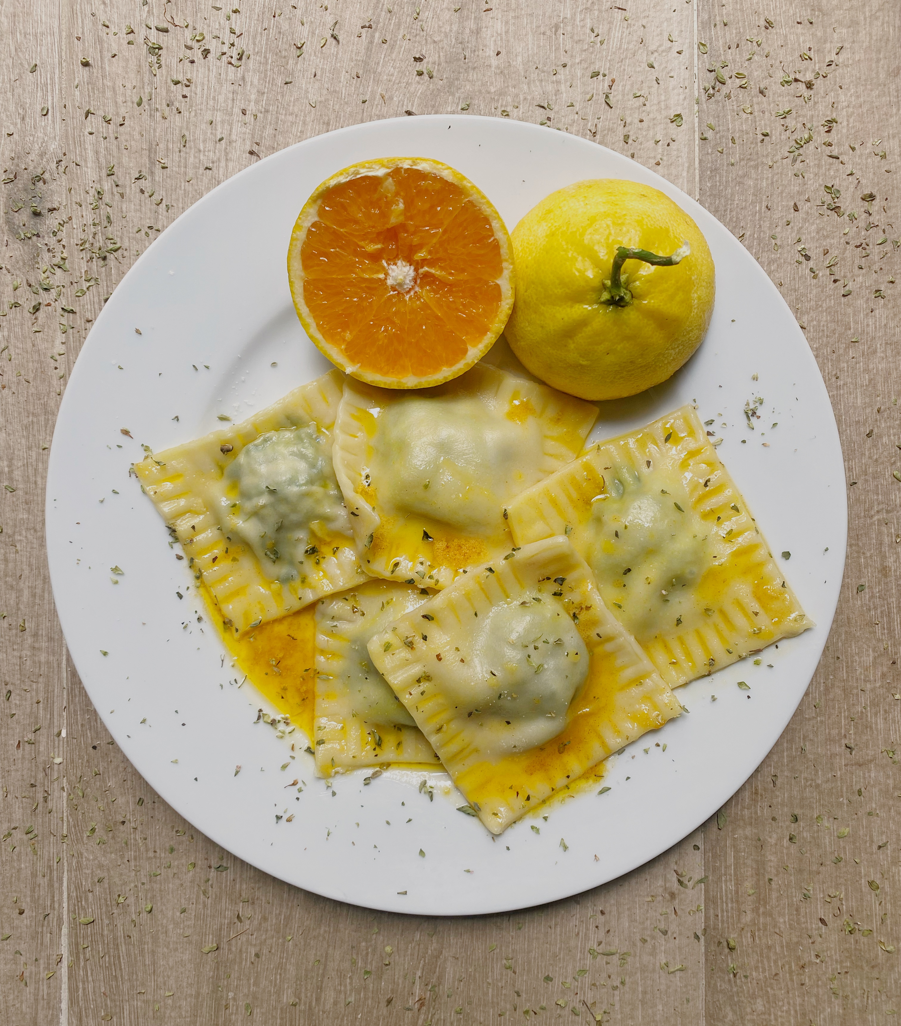 Almond Ricotta and Baby Spinach Ravioli with Orange Oil Drizzle (vegan) on a white plate, on grey surface